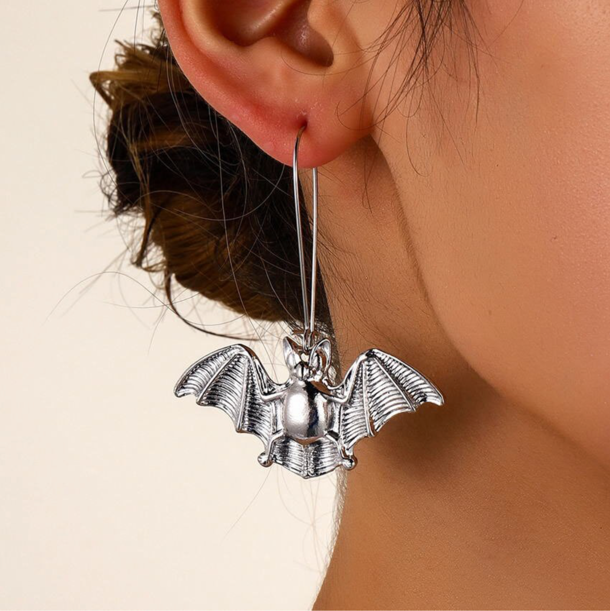 Silver-tone bat drop earring with spread wings, worn on an ear
