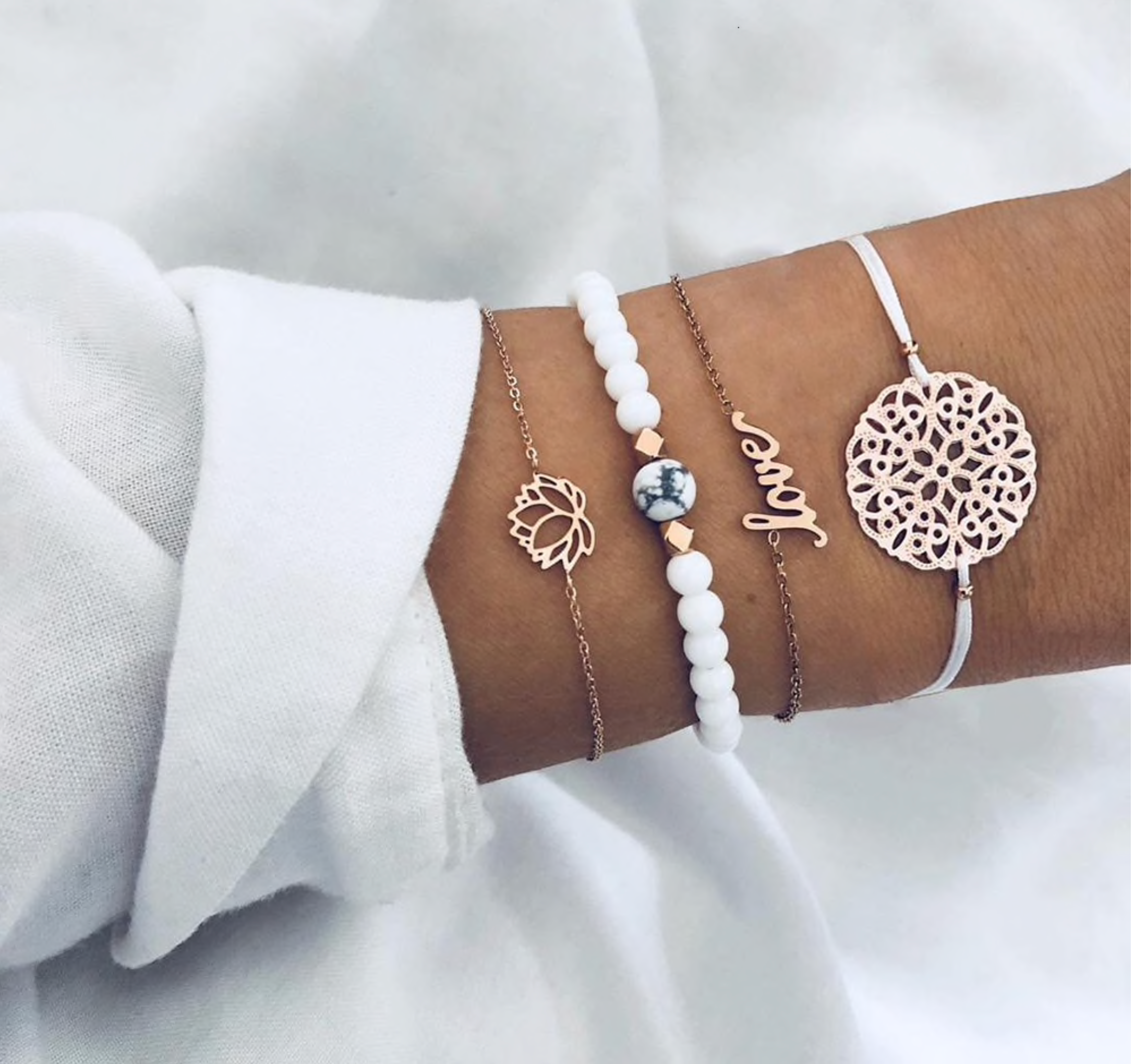 Model wearing white bead and rose goldtone bracelets with lotus and love charms