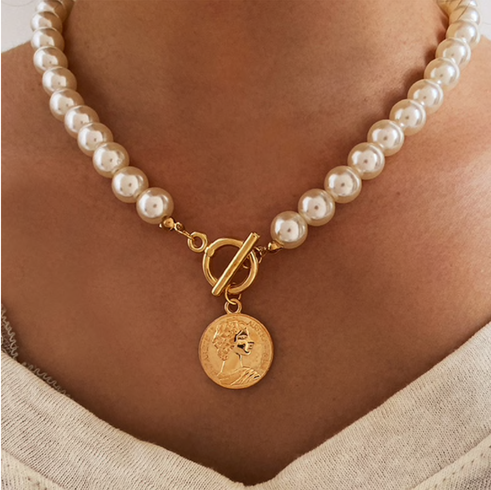 Model wearing an imitation pearl necklace with a goldtone toggle and medallion